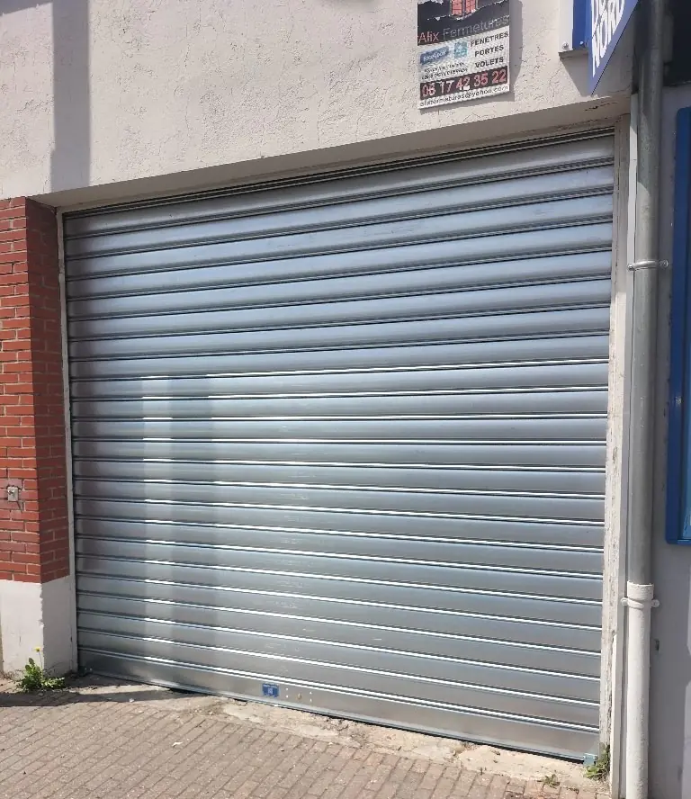 Installation d'un rideau métallique à lames pleines en acier galvanisé pour la sécurisation d'une devanture commerciale. Pose certifiée MGParis conforme aux normes de sécurité anti-effraction.