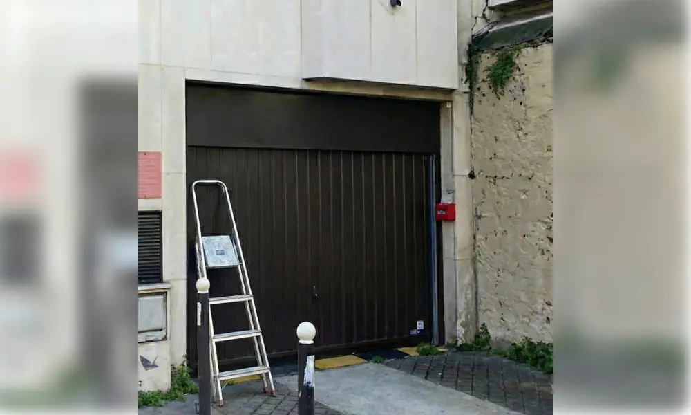 Porte de garage basculante sombre à nervures verticales à l’entrée d’un immeuble, à Châtenay-sur-Seine