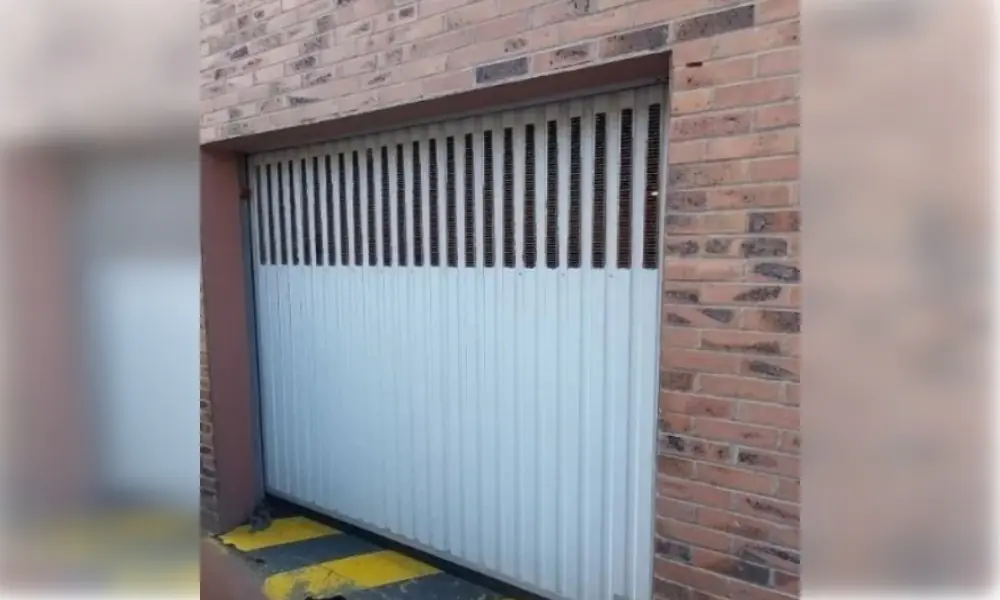 Porte de garage blanche à cannelures et ajours de ventilation, encadrée de briques rouges, Carnetin (77400)