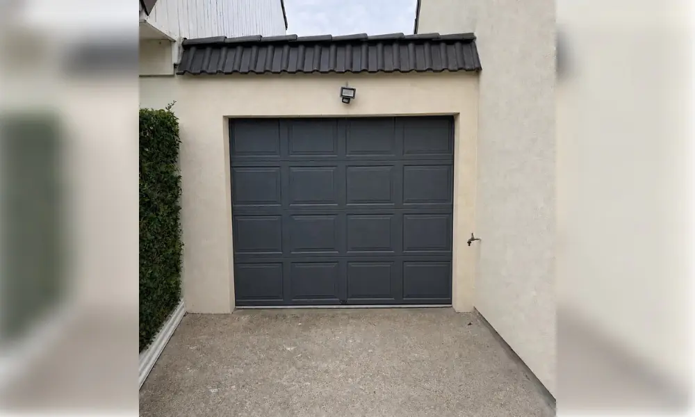 Porte de garage sectionnelle anthracite à cassettes sous un auvent de tuiles sombres, façade crépie beige, Coulommes