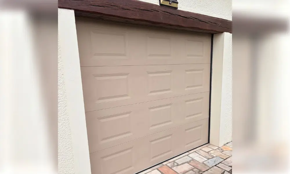 Porte de garage sectionnelle beige à cassettes sous un linteau en bois, maison de Champeaux