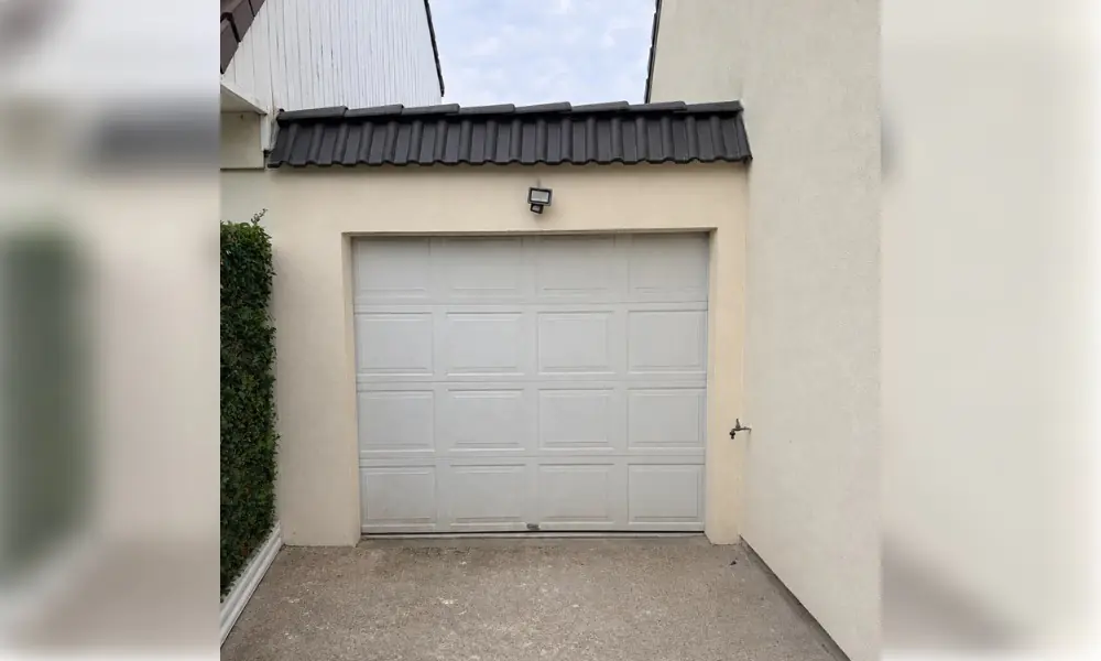 Porte de garage sectionnelle blanche à cassettes sous un auvent de tuiles sombres, Châteaubleau