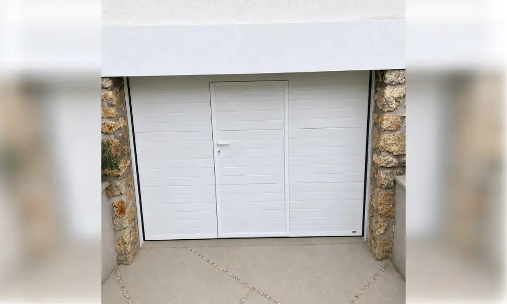 Porte de garage sectionnelle blanche à portillon intégré, encadrée de pierre ocre, à Châtenay-sur-Seine