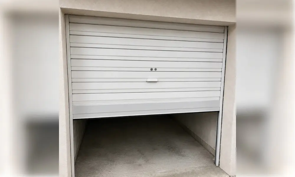 Porte de garage blanche à lames horizontales, légèrement relevée, dans un cadre crépi clair à Cuisy
